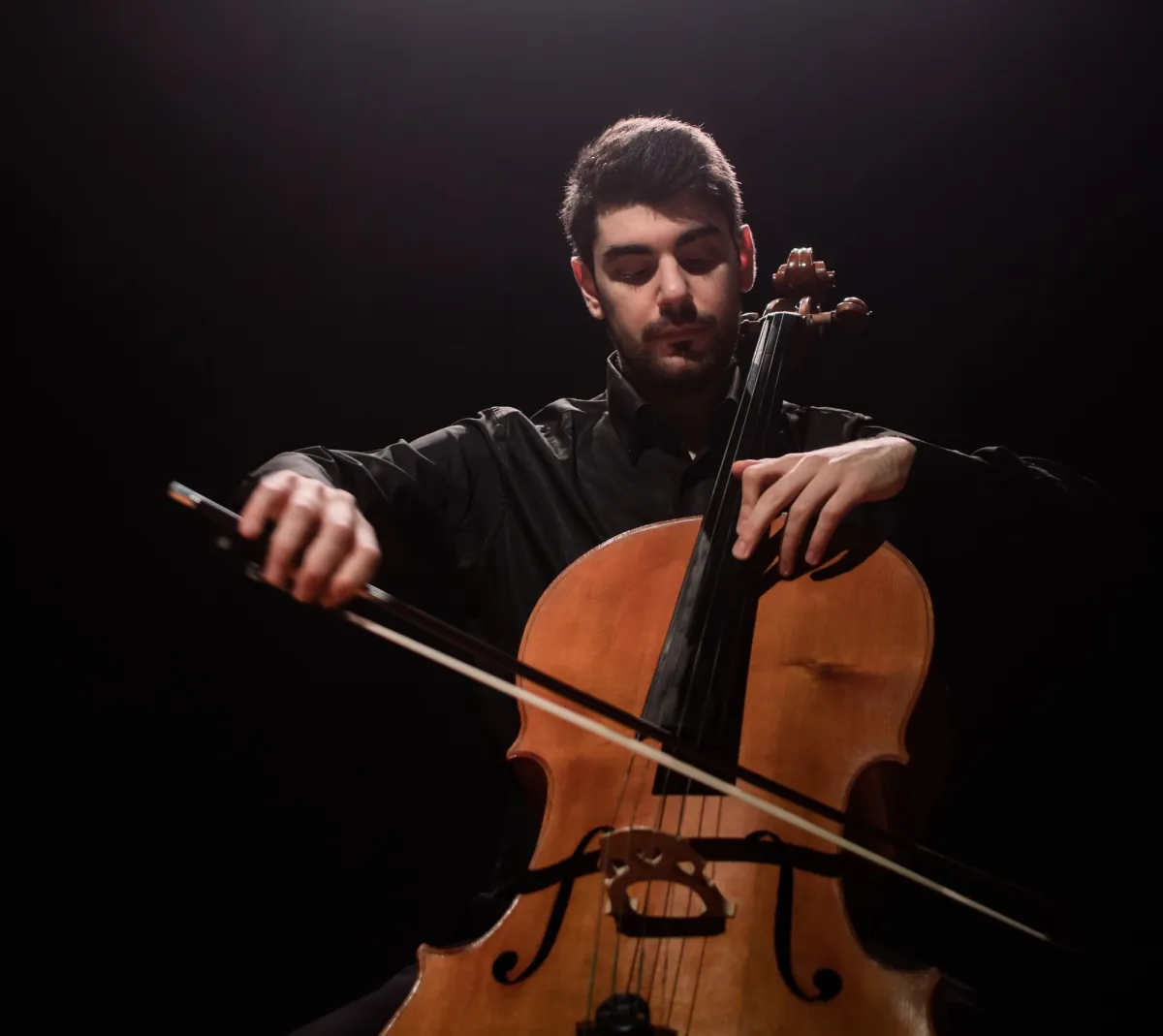 Claudio Aiello playing the cello on a dark stage