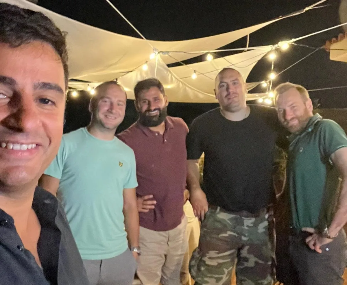 Five men smiling in a group selfie under string lights
