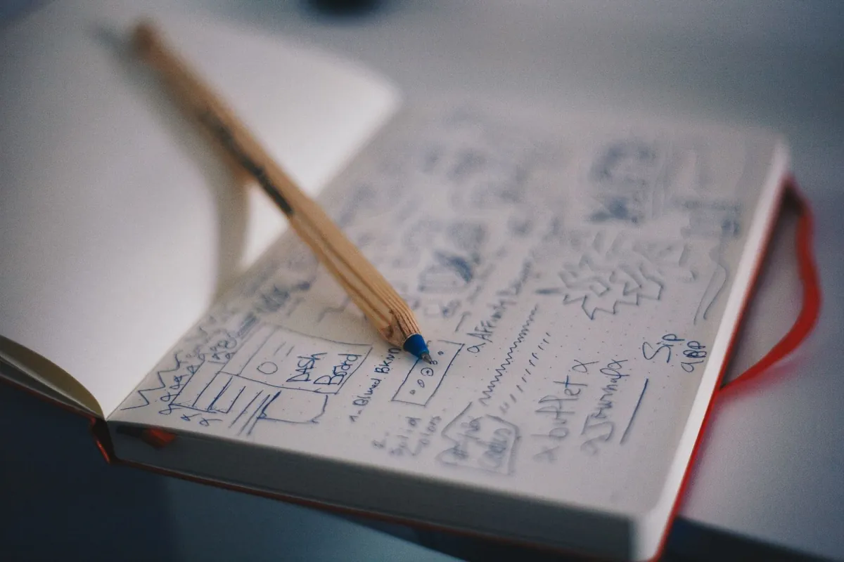 A notebook page of hand-drawn interface sketches, with a pencil resting on it